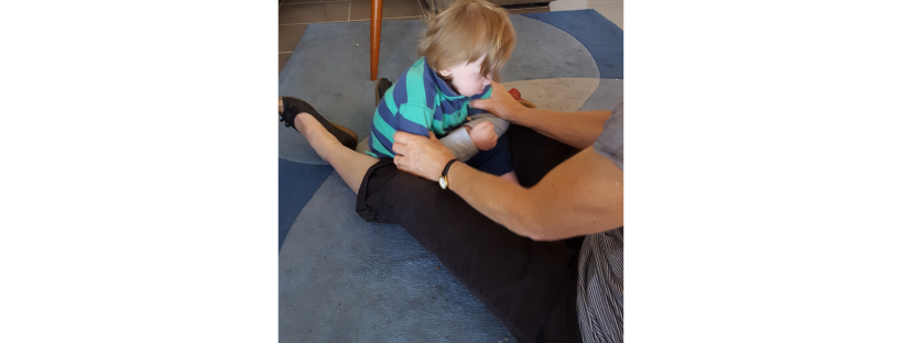 Physio-therapist - a great therapist - working wearing black pants and shoes, working with a young child wearing a green and blue striped shirt - practising sitting